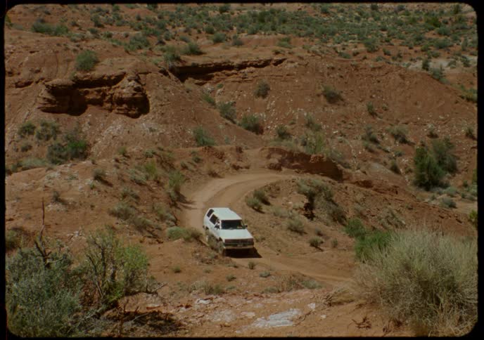 An off-road vehicle navigates a dusty, winding dirt road through a remote desert canyon
