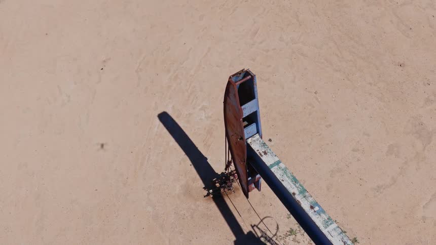 Top-down aerial view of a rusty, old oil pumpjack relentlessly working in the middle of a barren, sandy desert