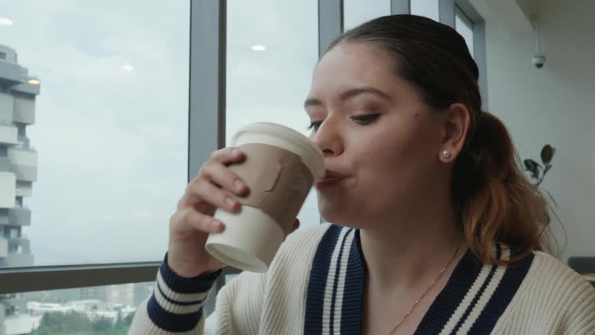 A young professional woman smiles as she works on her computer and enjoys a cup of coffee in a bright, modern office space