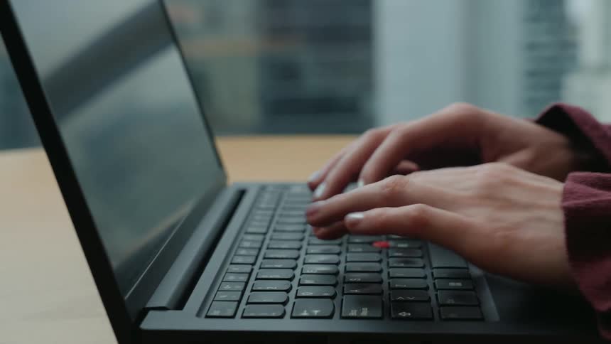 A close-up side view shows a person's hands swiftly typing on a sleek black laptop keyboard