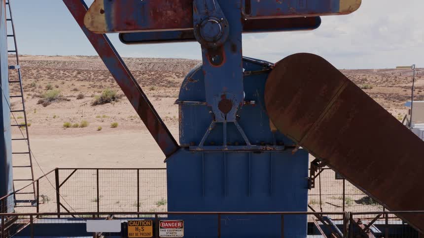 A close-up shot of a weathered and rusty oil pump jack's machinery operating in a desert