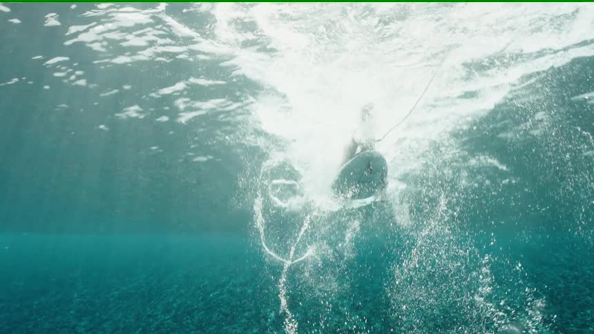 An ethereal underwater slow-motion view captures a surfer paddling before falling from their board into the clear turquoise ocean