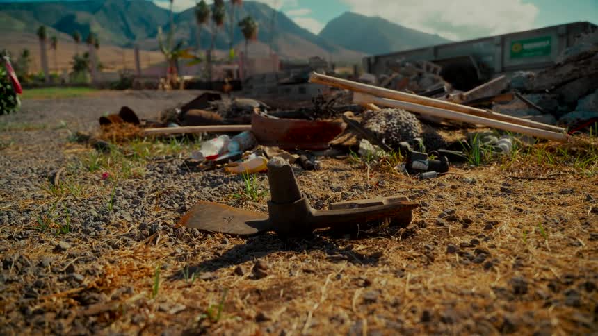 A rusty old plow blade lies abandoned on the ground in front of a pile of rubble and debris