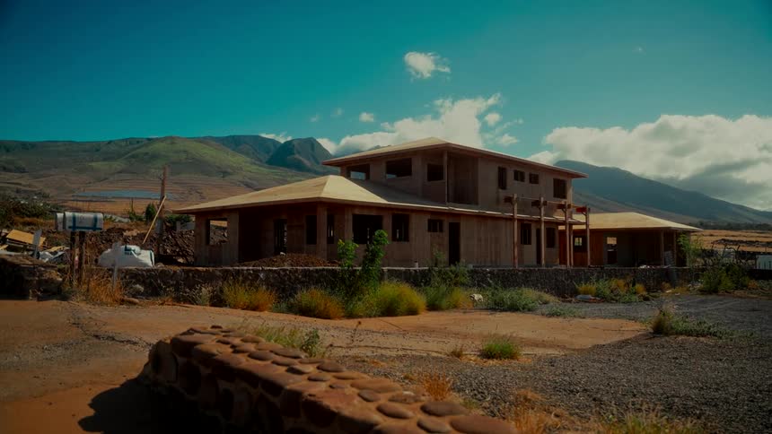 A time-lapse captures the construction of a new home in a vast, mountainous landscape on a sunny day
