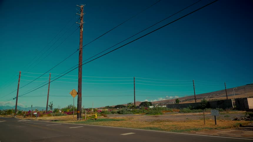 Telephone poles line an empty rural road under a vast, cloudless blue sky on a sunny day