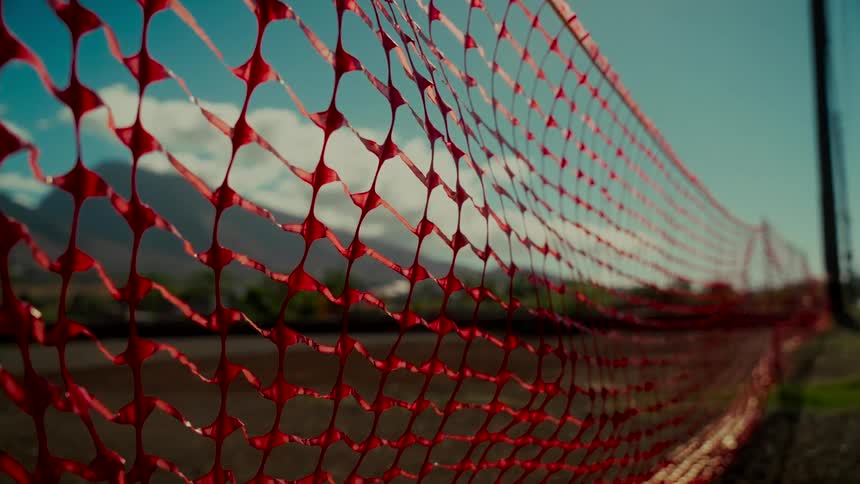 A red plastic safety fence creates a barrier in front of a distant mountain range under a partly cloudy blue sky