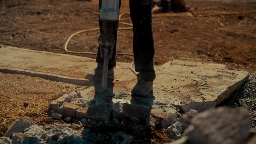 Low-angle slow motion shot of a construction worker using a jackhammer to break up a concrete slab