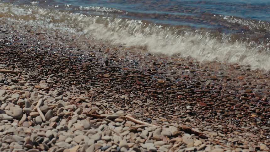 Gentle waves lap against a tranquil pebble shoreline on a sunny day