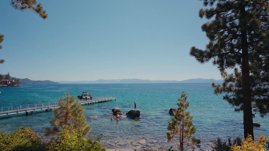 A tranquil, wide shot captures people swimming in the crystal-clear turquoise waters of Lake Tahoe next to a private pier