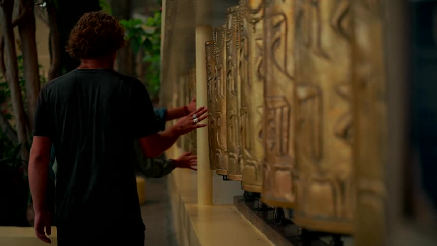 A couple gently spins a row of traditional golden Tibetan prayer wheels at a spiritual temple