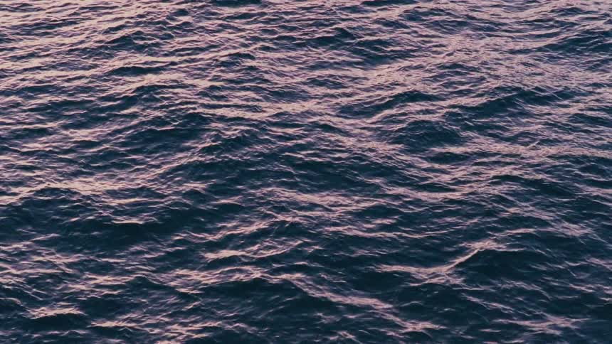 A serene top-down view of gentle ocean waves reflecting the soft purple and pink light of dusk