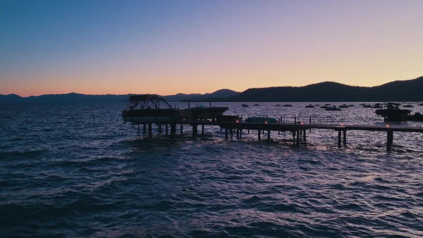 Gentle waves lap against a silhouetted wooden pier with docked boats under a beautiful twilight sky over a lake
