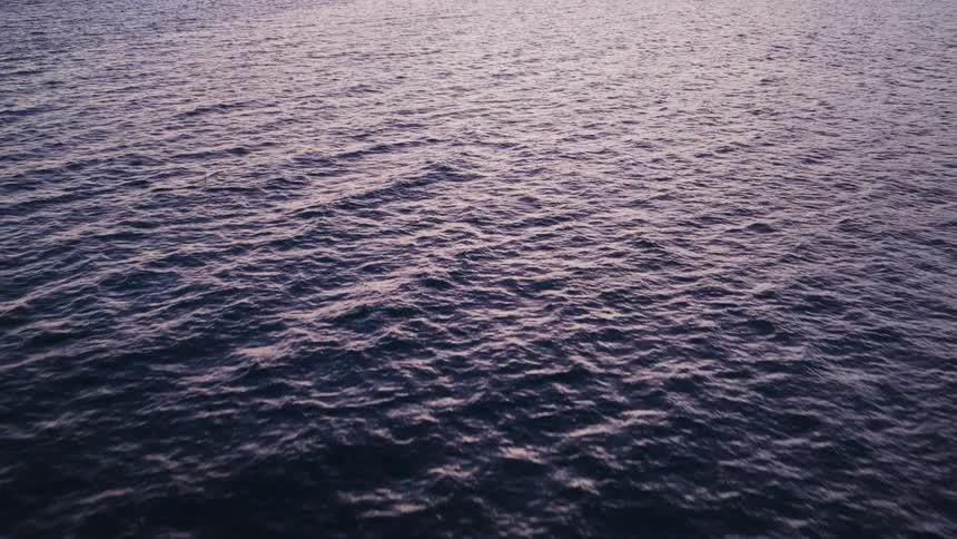 A slow aerial pullback over a vast expanse of calm, rippling water at twilight