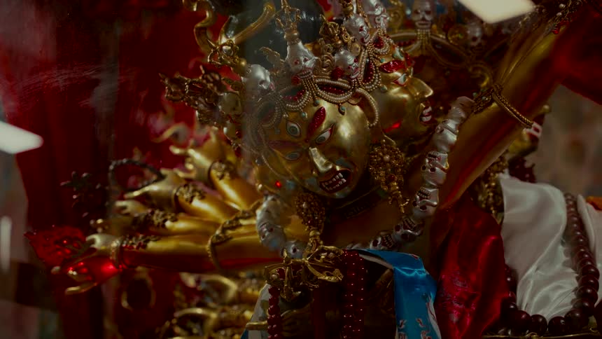 Mystical light plays across the fierce golden face of a multi-headed Tibetan Buddhist deity statue