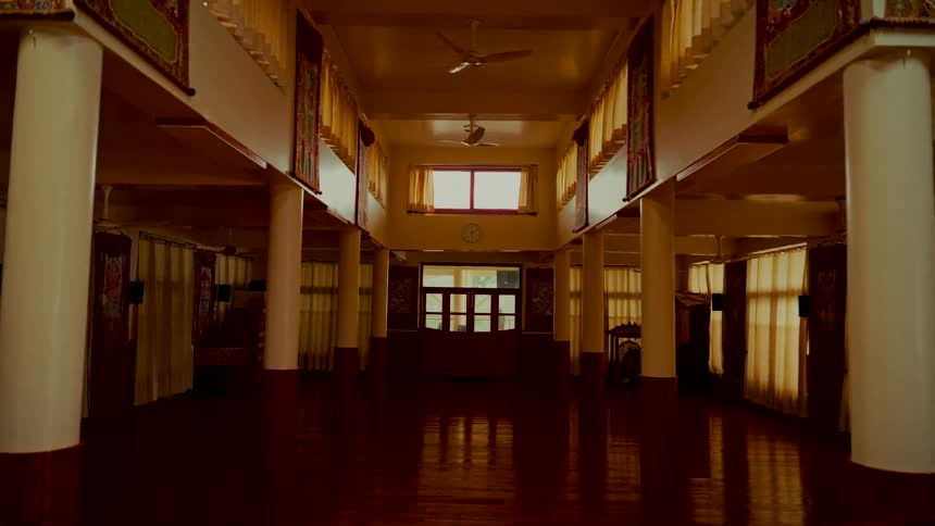Sunlight filters through the windows of a large, empty, and serene Buddhist monastery prayer hall with polished wooden floors