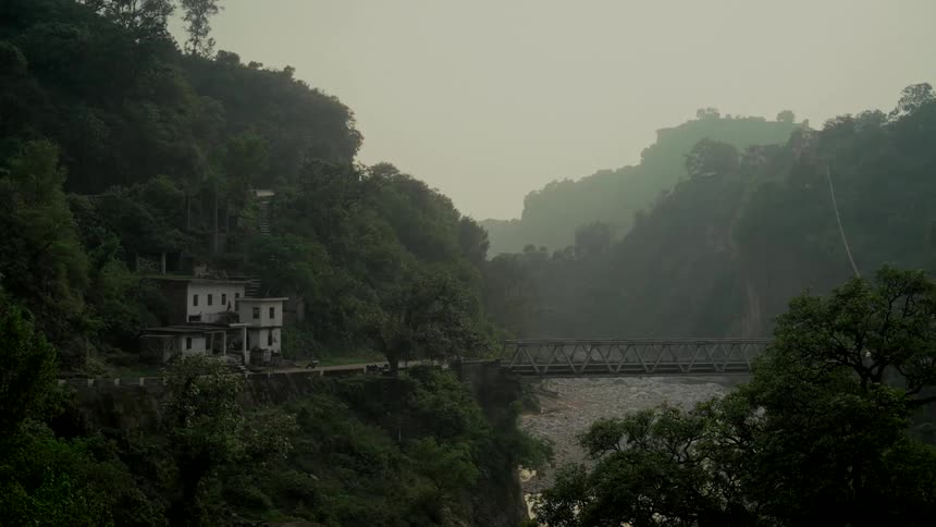 A scenic view of a river flowing under a truss bridge through a lush, misty mountain valley