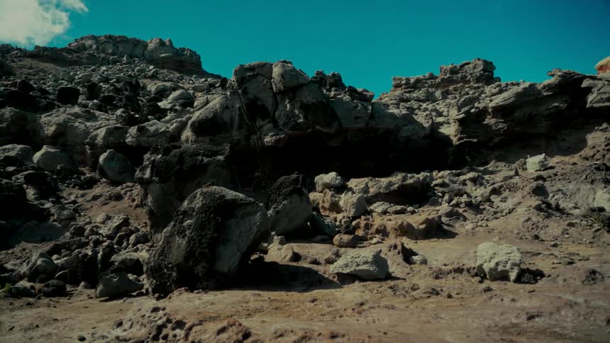 A slow pan reveals a desolate and rocky badlands terrain under a harsh, sunlit sky