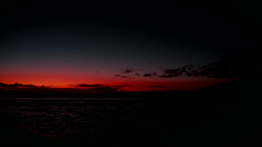 A vibrant crimson sunset glows on the horizon over a dark and tranquil ocean at twilight