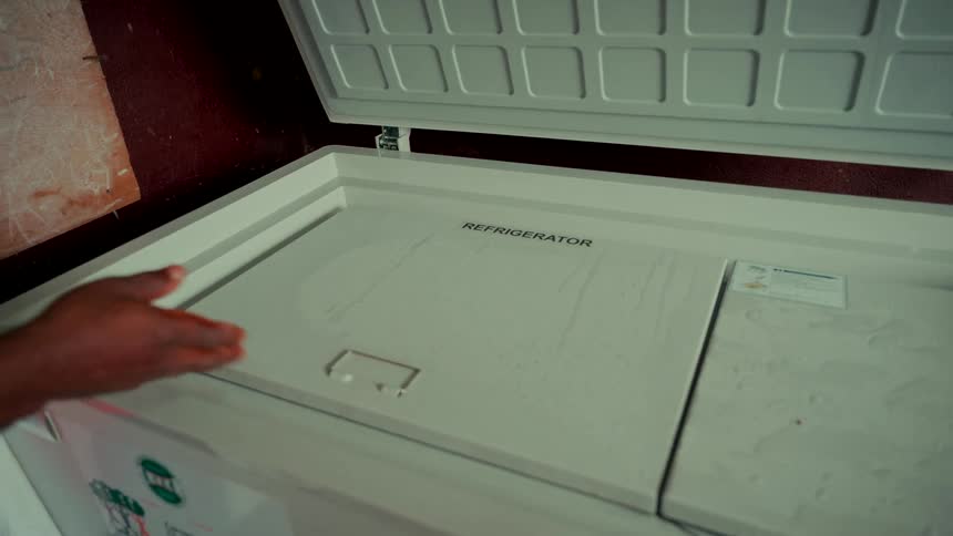 A medical worker in a white coat opens the double lid of a medical-grade chest refrigerator in slow motion
