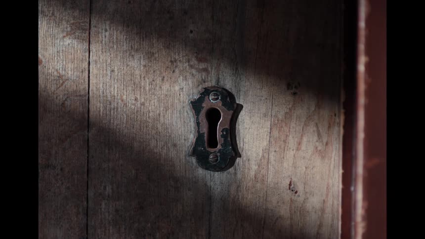 A mysterious light seen through an old keyhole is suddenly extinguished as a shadow passes over the door