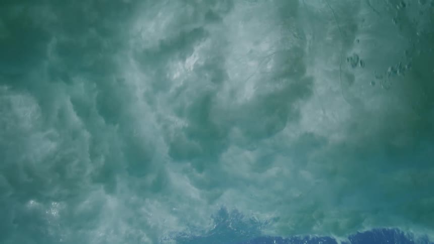 An amazing underwater view captures a powerful ocean wave breaking overhead in slow motion with the sun shining through