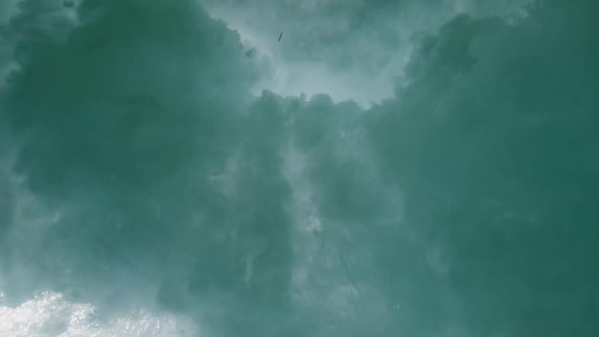 An underwater view in slow motion as a powerful ocean wave breaks overhead, filling the screen with turbulent water and bubbles