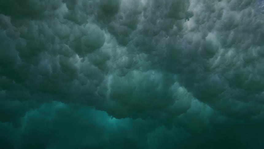 An incredible slow-motion underwater view of a powerful ocean wave breaking overhead, creating a turbulent cloud of whitewater