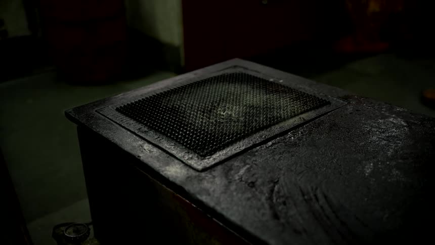 A hand slowly removes a stained orange rag from a dark, grimy metal surface in a dimly lit room