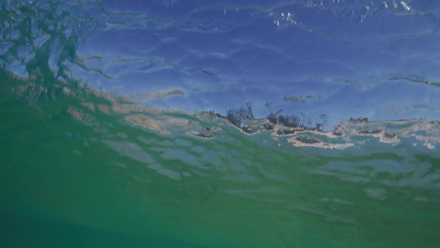 An immersive underwater view captures a powerful ocean wave as it gracefully curls and breaks overhead in slow motion