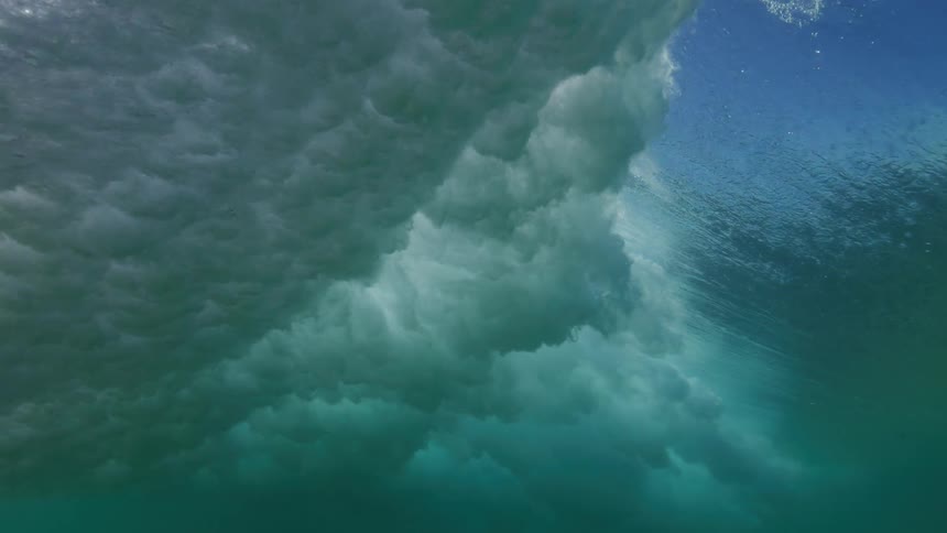 An epic slow motion underwater shot captures a powerful turquoise ocean wave crashing overhead