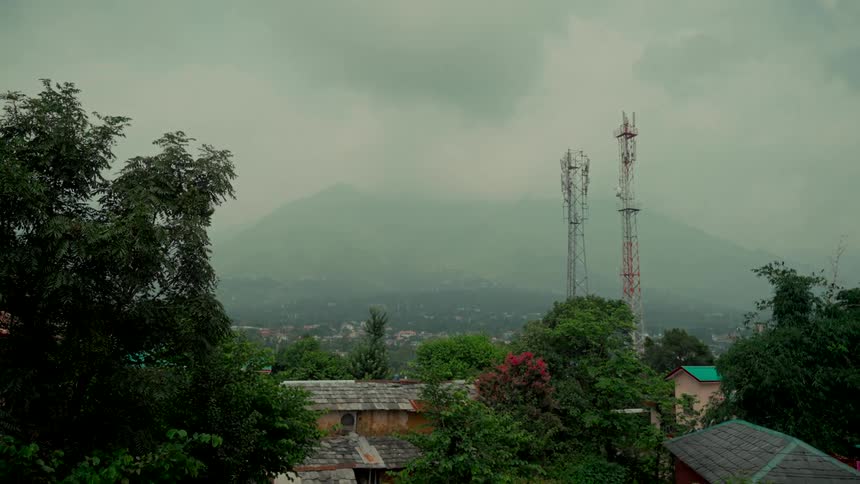 Communication towers stand amidst lush trees in a mountain town on a foggy, overcast day