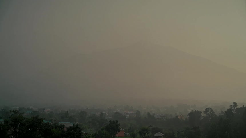 A powerful thunderstorm with lightning flashes and torrential rain engulfs a town in a mountain valley