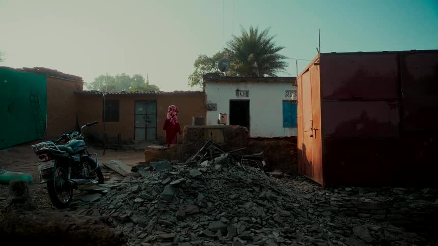 A woman in a red sari walks through the dusty courtyard of a rural village home