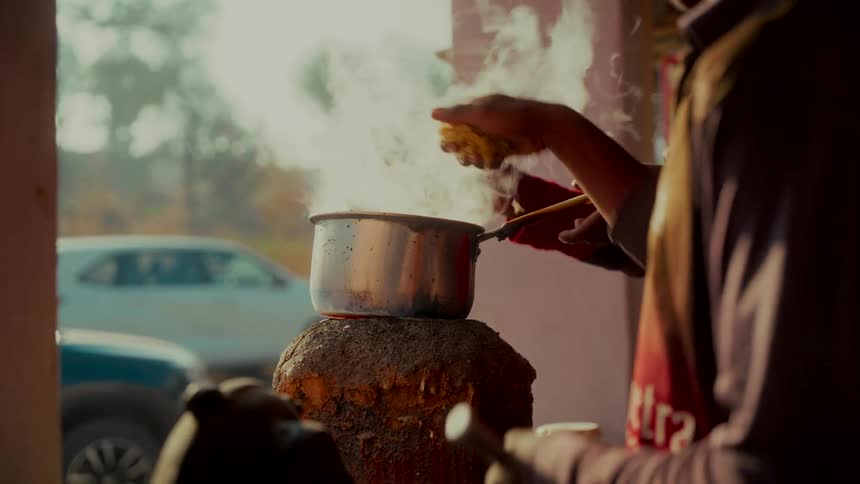 Slow motion close-up of a street vendor stirring a pot of steaming hot traditional Indian masala chai on a rustic stove