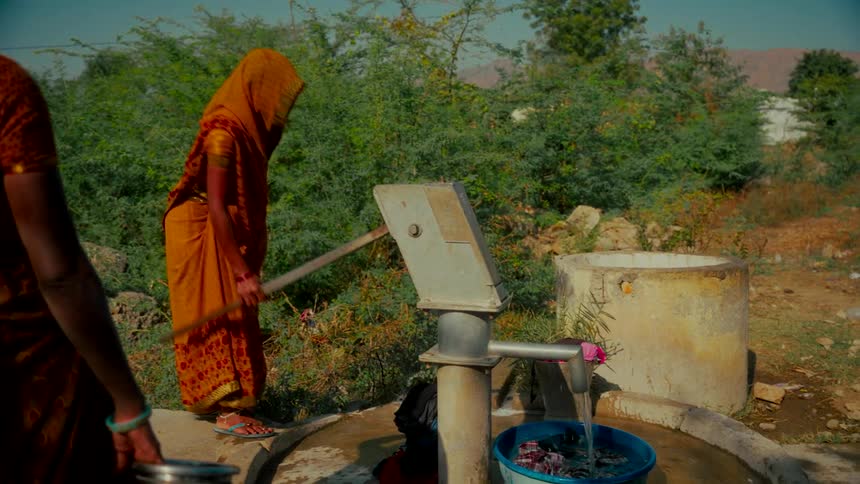 A woman in a colorful sari pumps water from a hand pump in a rural Indian village