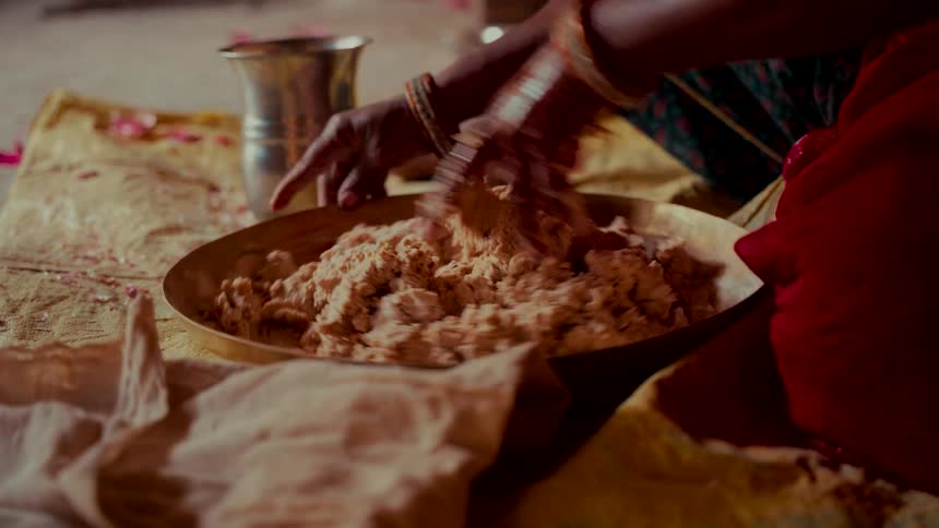 An Indian woman kneads dough by hand in a brass bowl while preparing a traditional meal