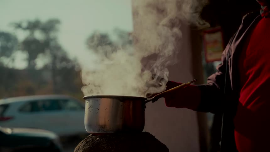 Slow motion close-up of a person preparing traditional hot chai tea in a steaming pot at a roadside stall