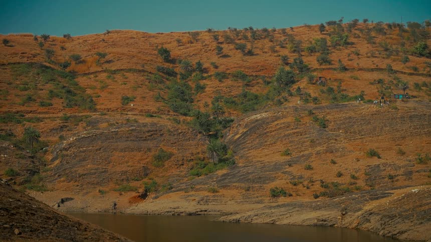 A tranquil view of a lake nestled among dry, rolling hills under a clear sky