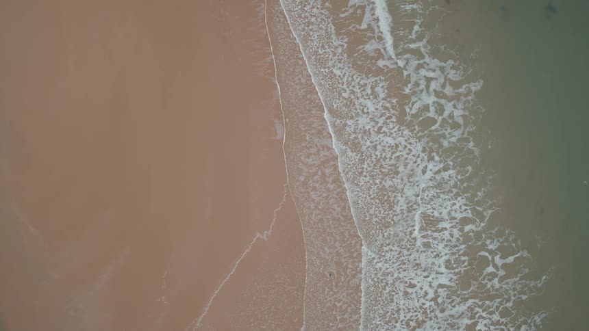 A serene top-down aerial view of ocean waves gently washing ashore on a sandy beach
