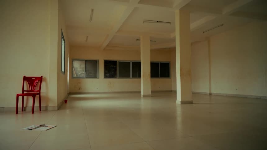 A solitary red chair stands in the corner of a large, empty, derelict room, creating a sense of isolation and abandonment