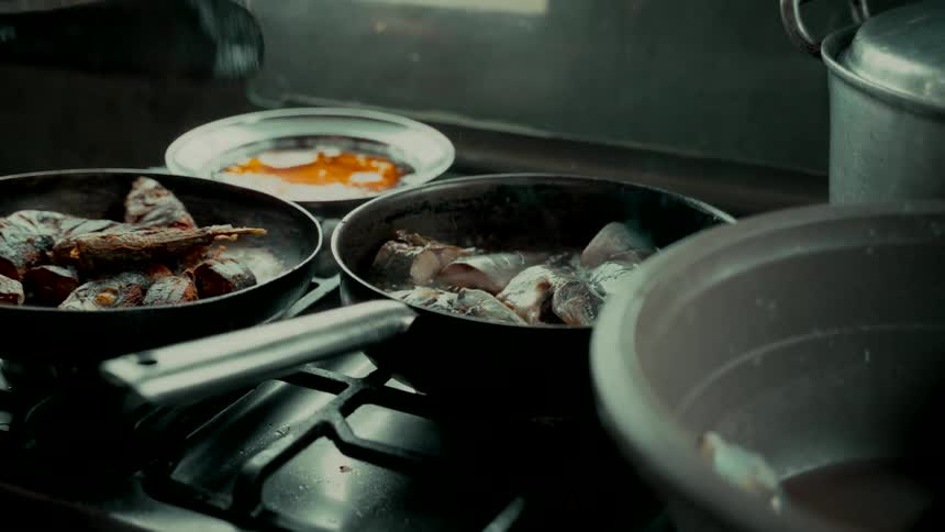A chef fries fresh fish filets in a hot pan on a stove in a bustling kitchen