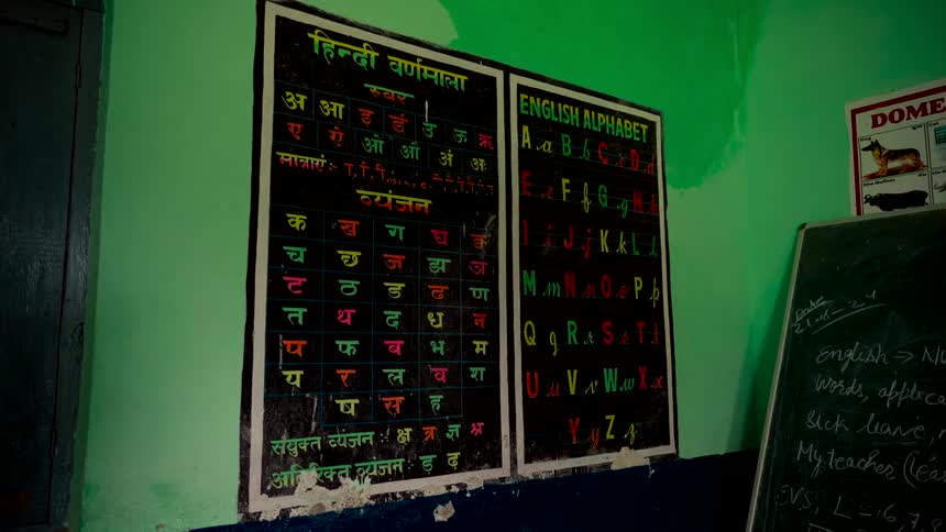 Educational posters of the Hindi and English alphabets hang on a weathered green classroom wall in an Indian school