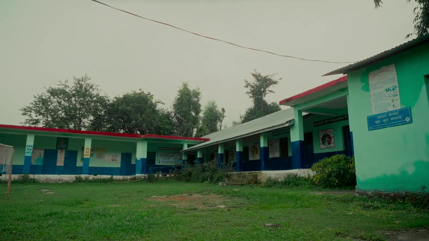 The empty, grassy courtyard of a rural Indian school building on a gloomy, overcast day