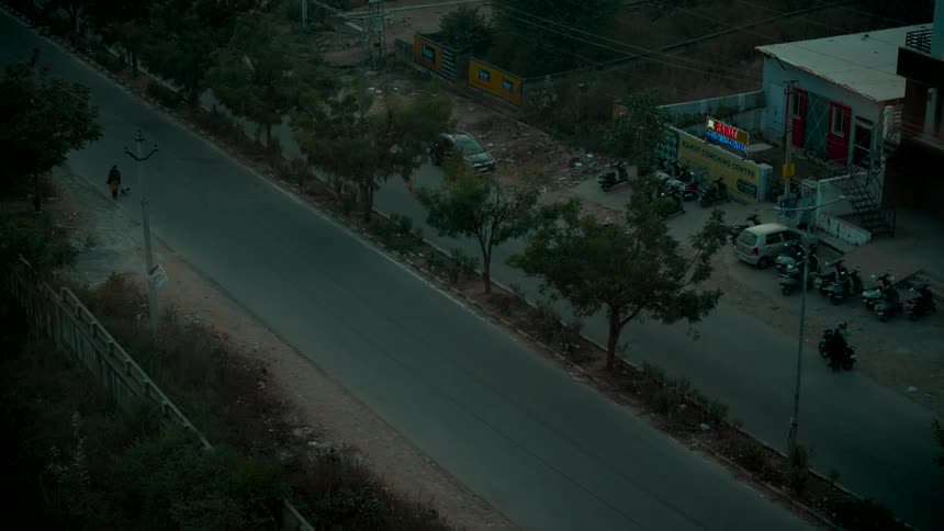 An elevated view of a quiet street with sparse traffic of scooters and cars passing by at dusk