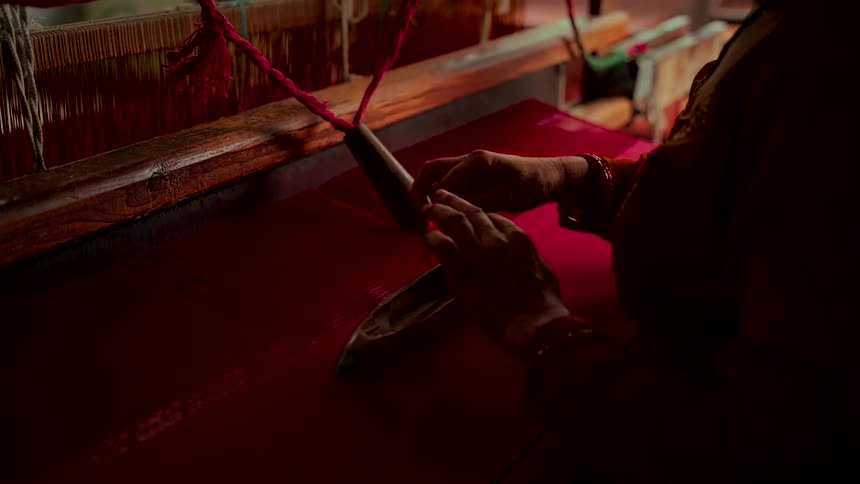 An artisan carefully changes the thread on a handloom shuttle while weaving a vibrant red textile