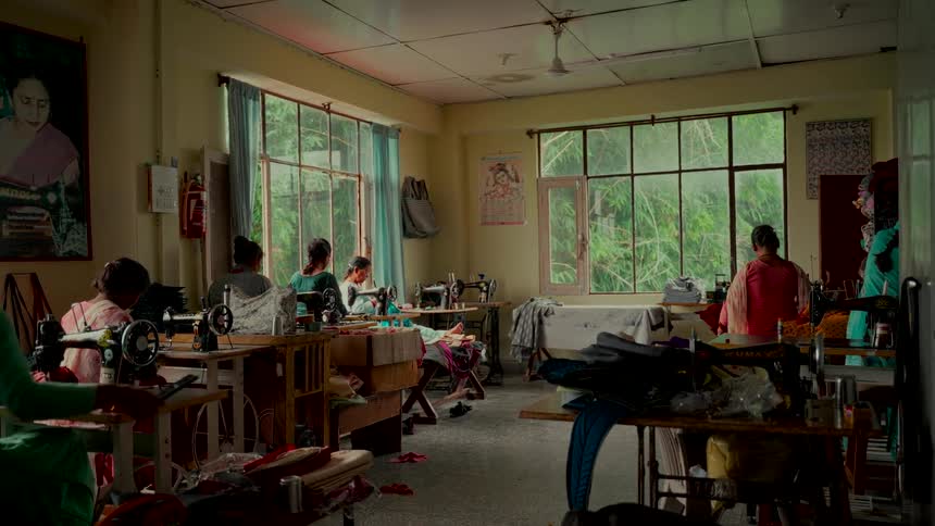 A group of women in a South Asian sewing cooperative diligently work at their machines in a room filled with natural light