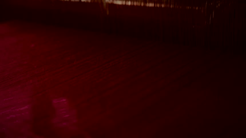 A detailed close-up shot captures a weaving loom in action, creating a vibrant red textile