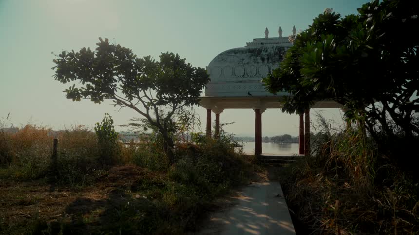 A tranquil view of a traditional Indian chhatri pavilion overlooking a serene lake on a hazy day
