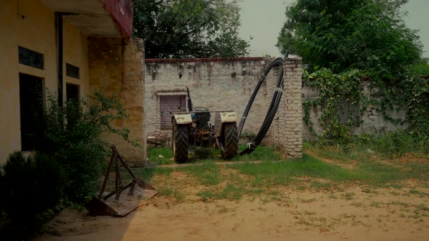 A white tractor sits parked in the grassy, sandy backyard of a rural village home
