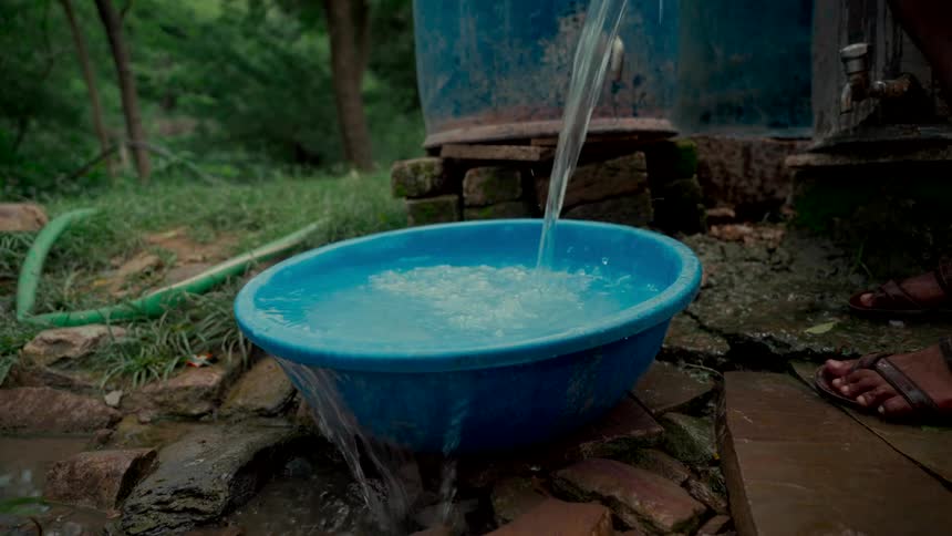 Slow motion shot of fresh water being poured into a blue basin until it overflows onto the rustic ground